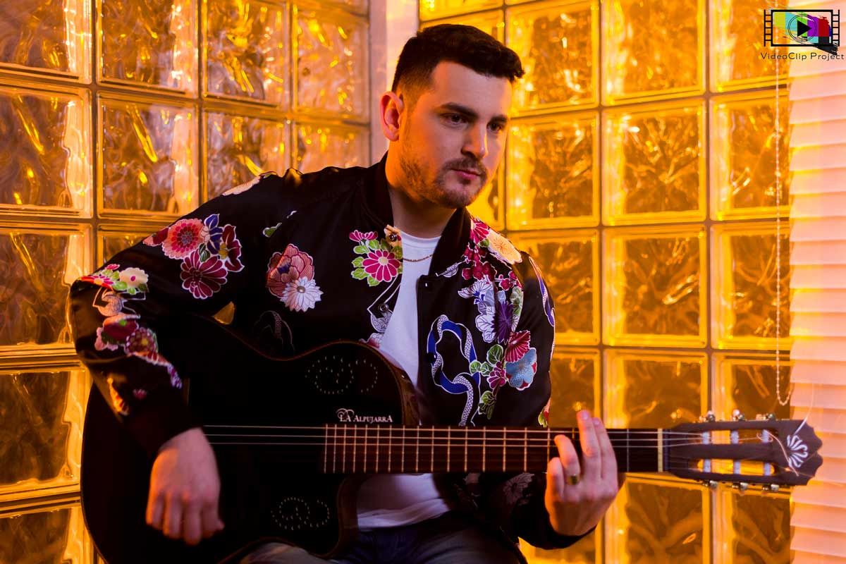 Lisandro Machado tocando la guitarra frente a una pared de vidrios de color ámbar